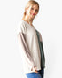 A woman modeling a color-blocked ribbed knit sweater with a cream body, taupe sleeves, and a muted green panel on the front, paired with blue jeans against a plain white background.