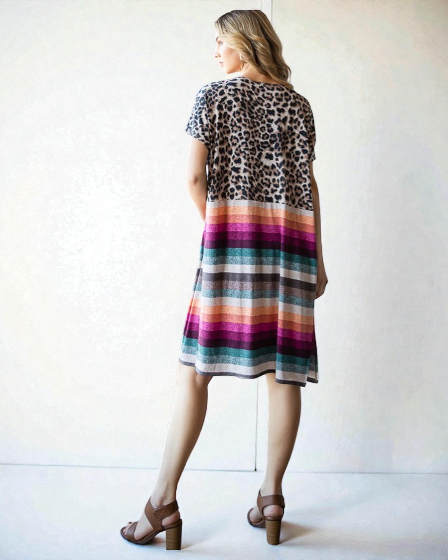 Woman wearing a dress with a leopard print top and colorful striped skirt against a white background