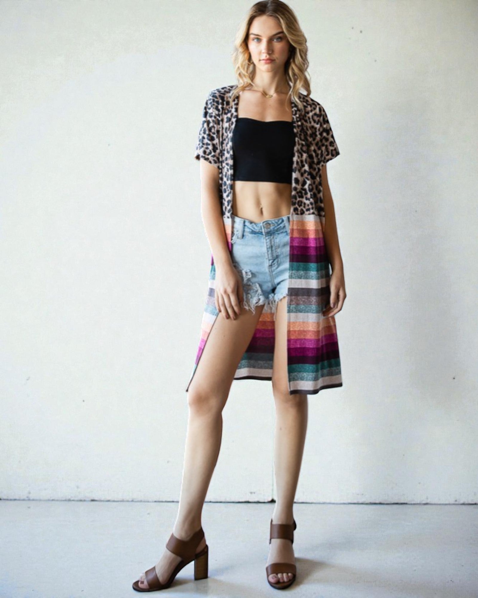 Woman wearing a leopard print shirt, black crop top, denim shorts, and a colorful skirt against a white background.