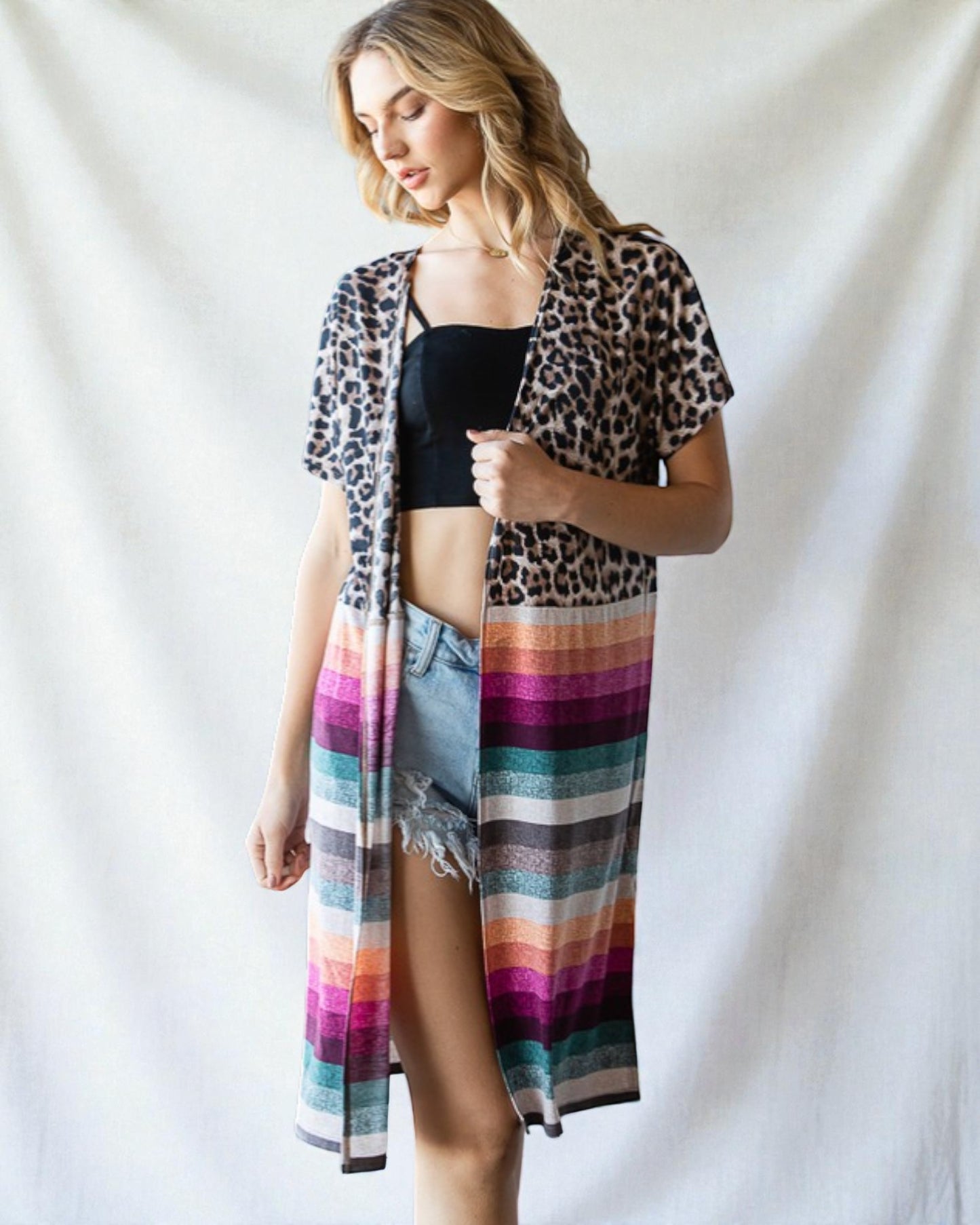 Woman wearing a leopard print cover-up with a colorful striped skirt over a black top on a white background