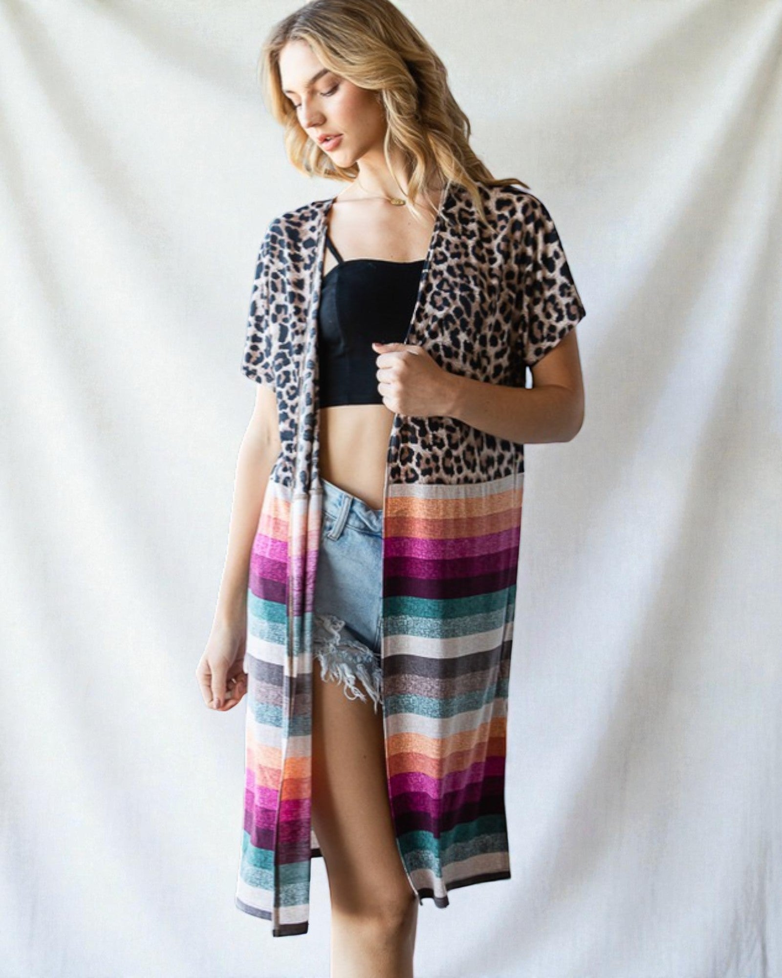 Woman wearing a leopard print cover-up with a colorful striped skirt over a black top on a white background