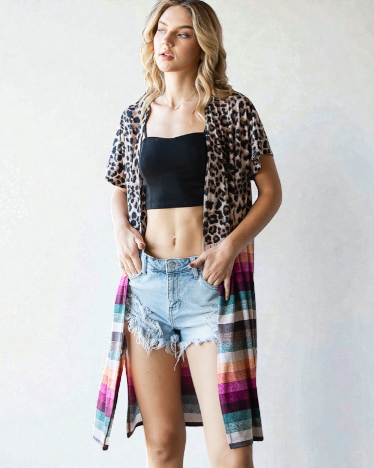 Woman wearing a leopard print shirt over a black crop top and denim shorts on a white background