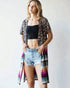 Woman wearing a leopard print shirt over a black crop top and denim shorts on a white background