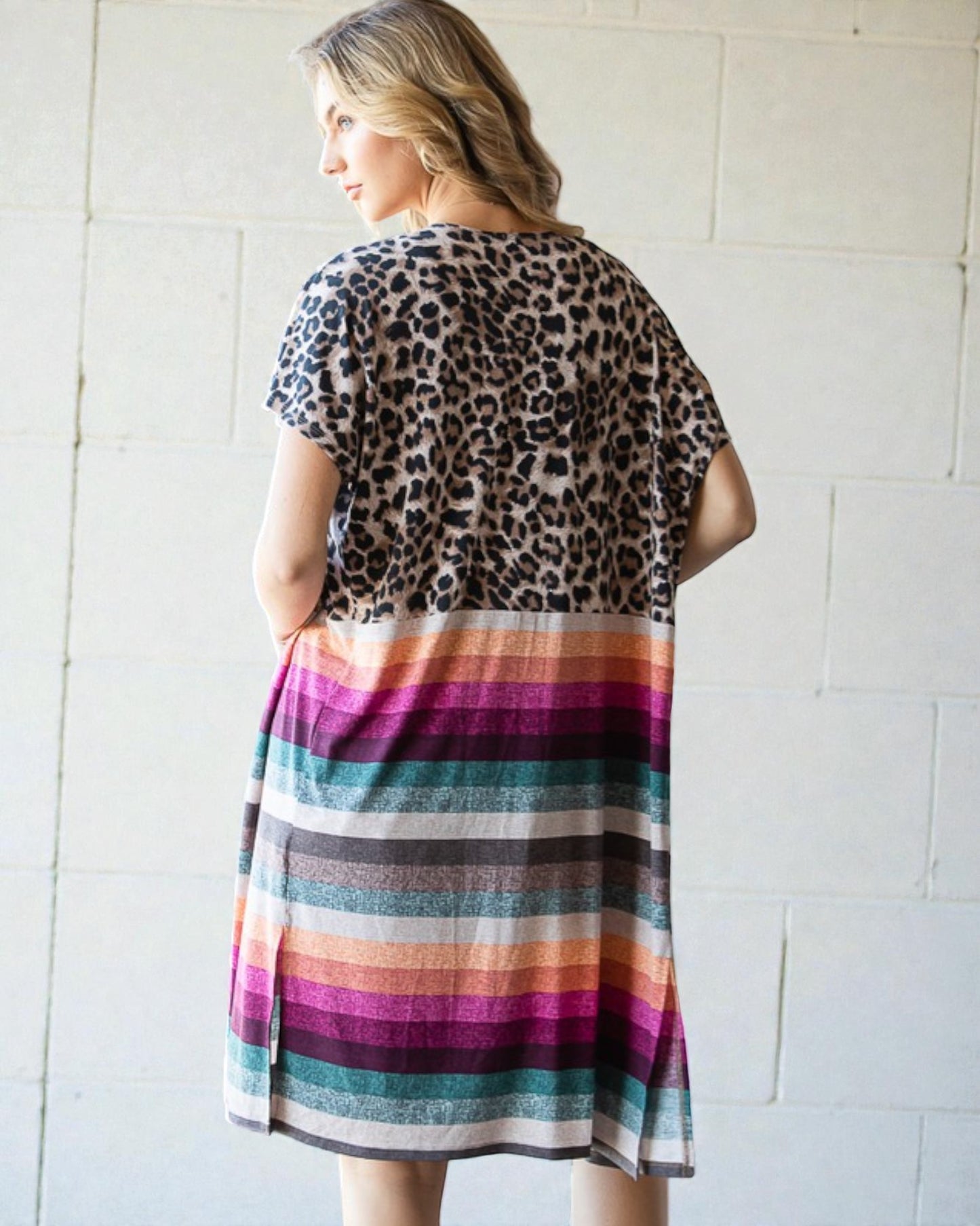 Woman wearing a dress with leopard print top and colorful striped skirt against a white tiled wall.