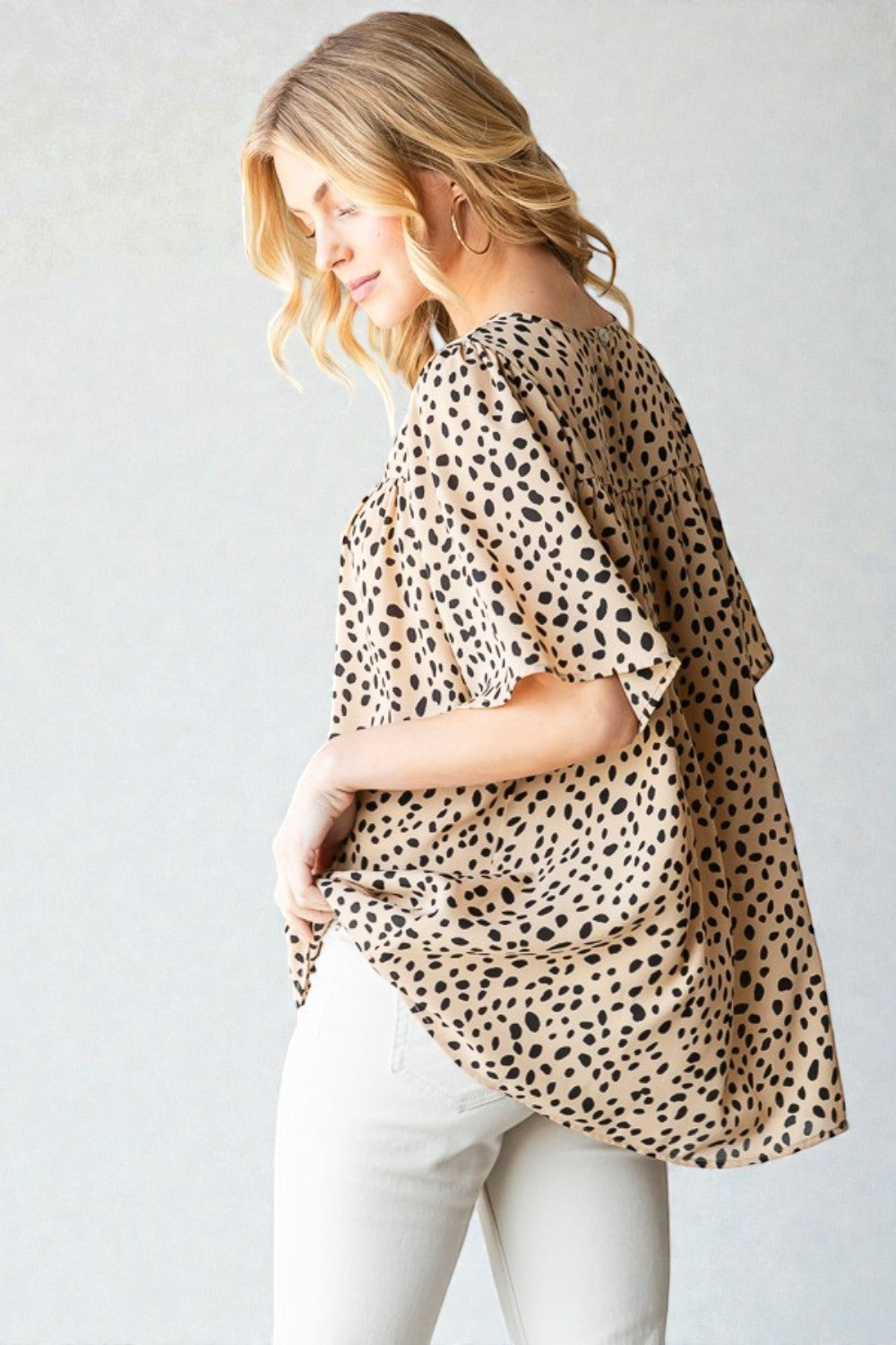 Woman wearing a leopard print top and white pants against a plain background