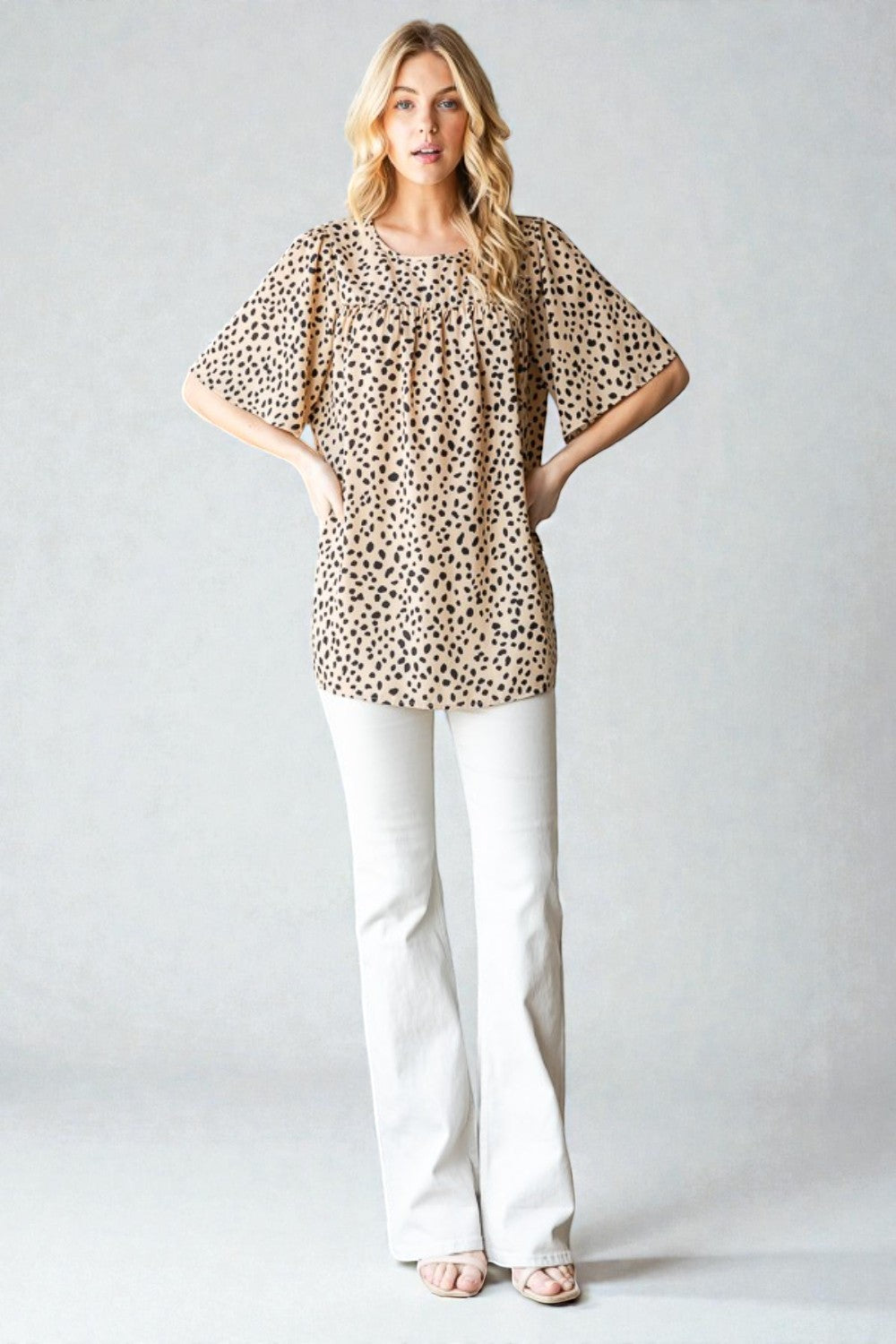 Woman wearing a leopard print top and white pants on a plain background