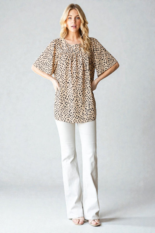 Woman wearing a leopard print top and white pants on a plain background