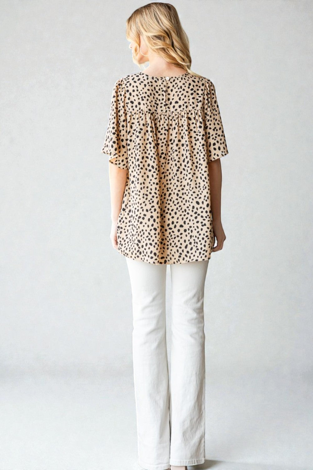 Woman wearing a leopard print top and white pants against a plain background