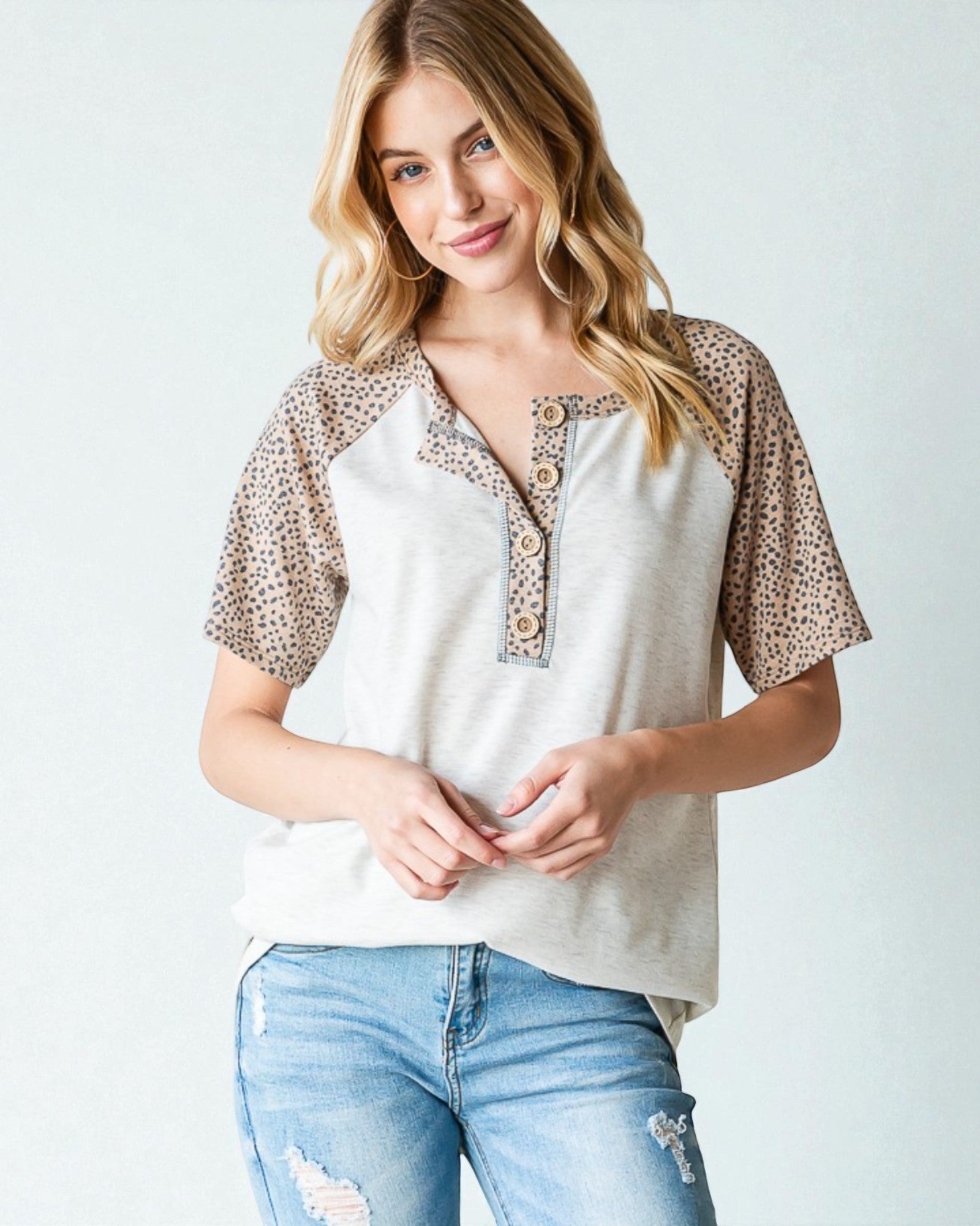 Woman wearing a white blouse with leopard print sleeves and blue jeans on a light background