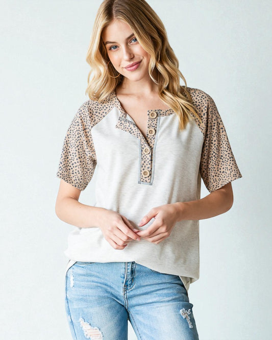 Woman wearing a white blouse with leopard print sleeves and blue jeans on a light background