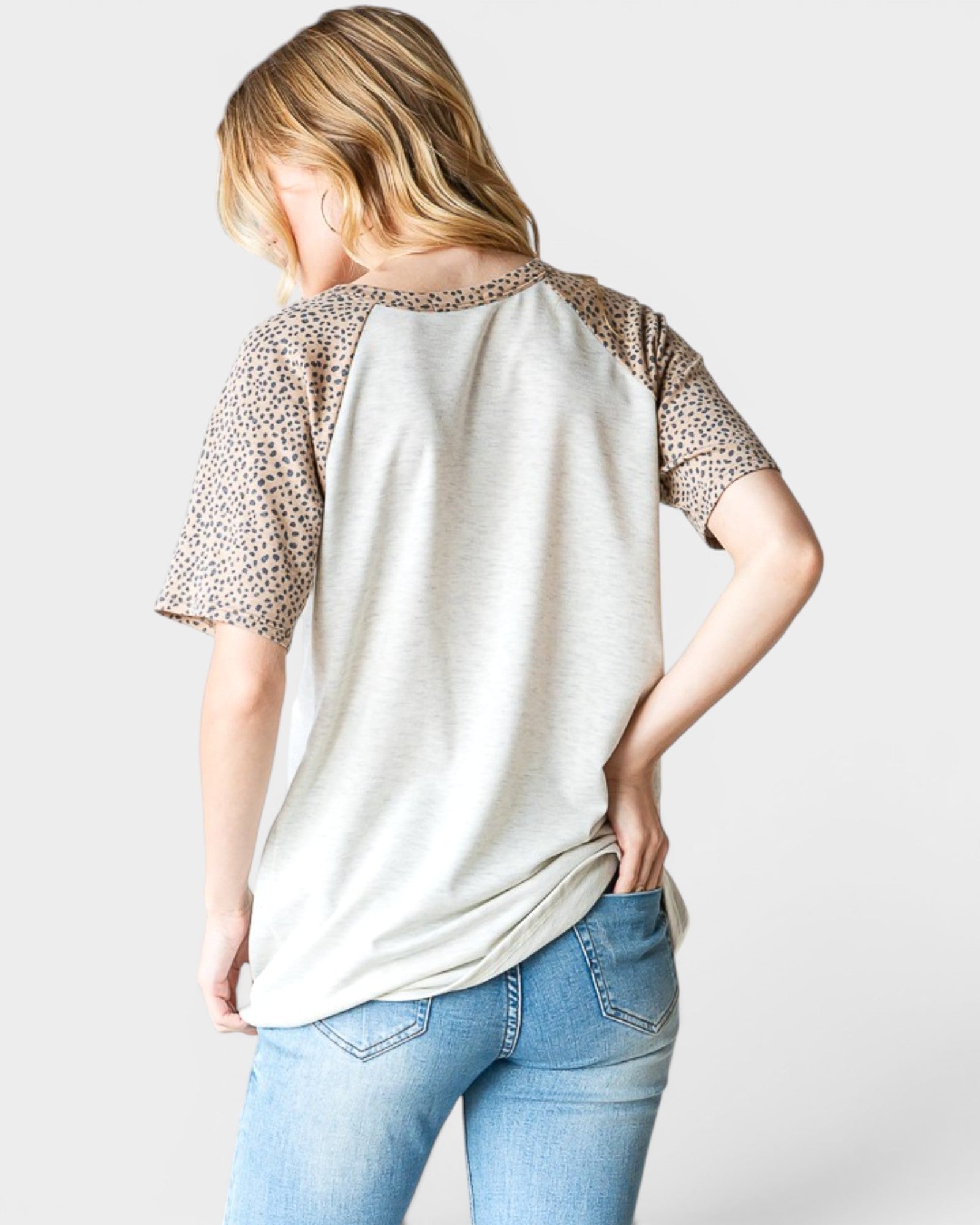 Woman wearing a beige and leopard print top with blue jeans on a white background