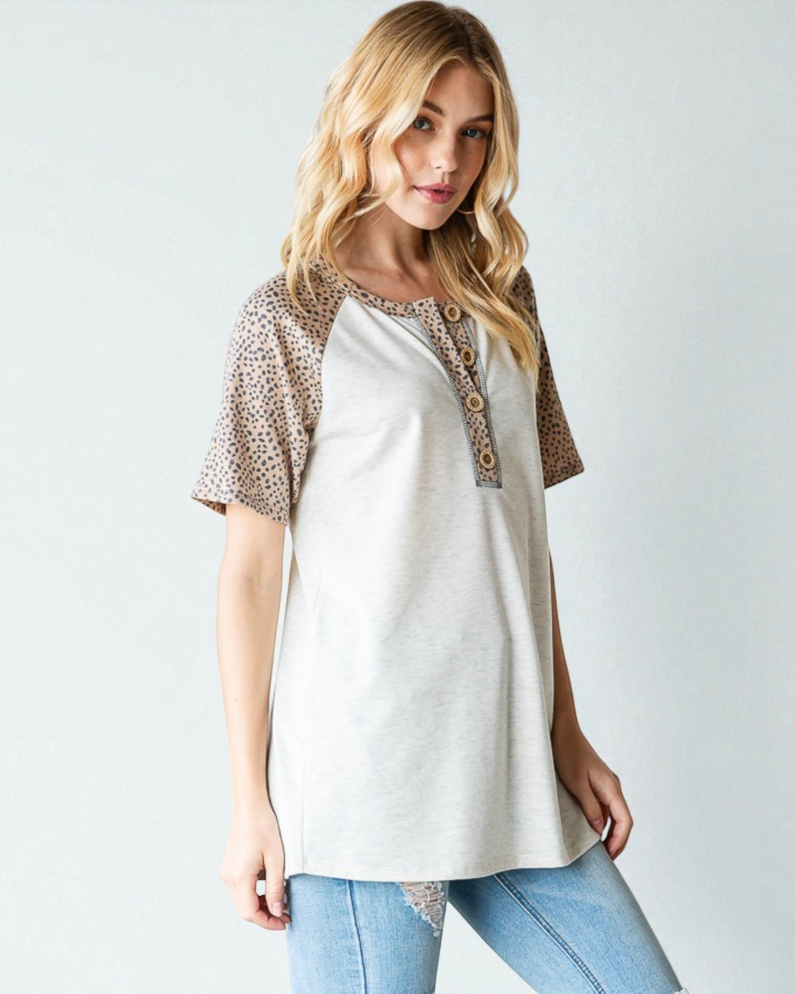 Woman wearing a white top with leopard print sleeves on a plain background