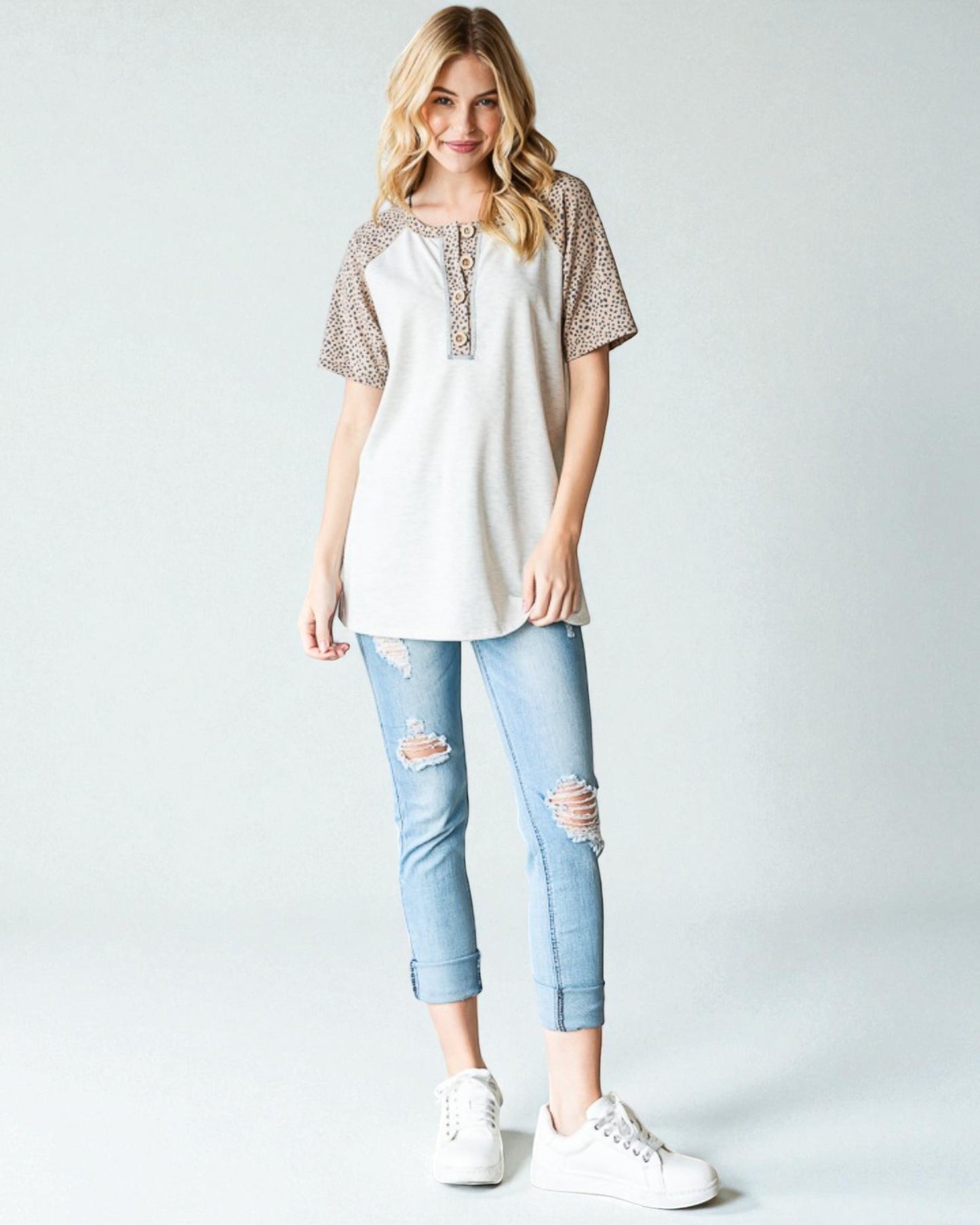 Woman wearing a white top with lace sleeves and light blue jeans on a plain background