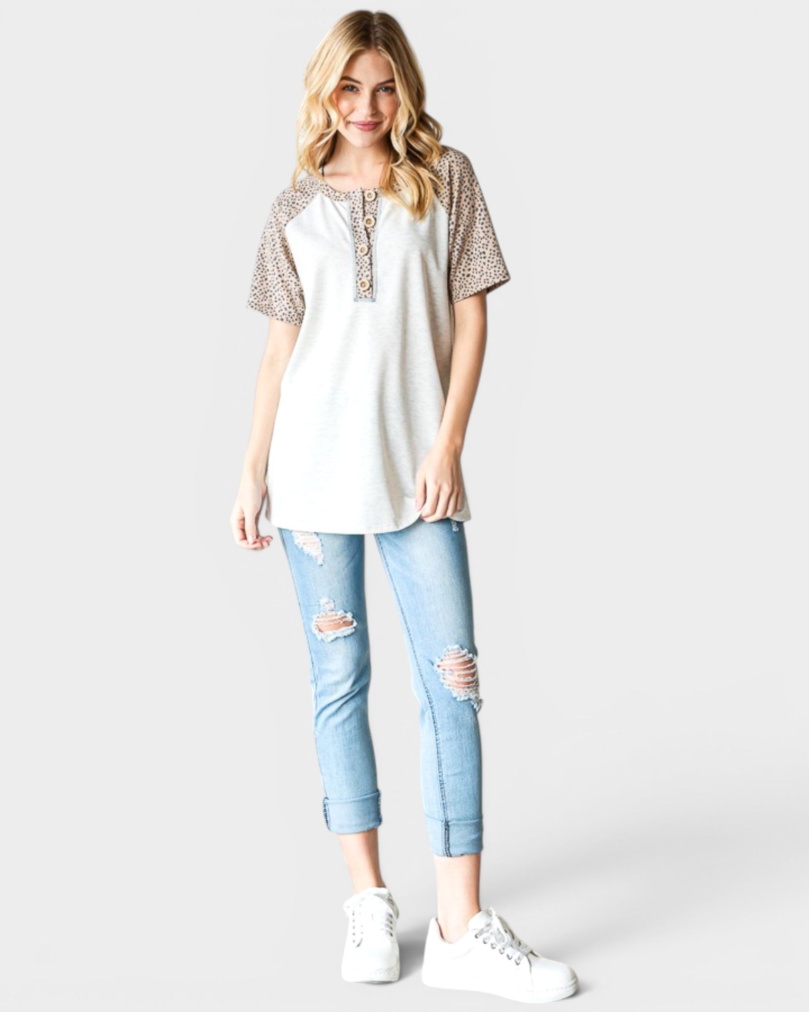 Woman wearing a white top with leopard print sleeves and light blue jeans on a white background