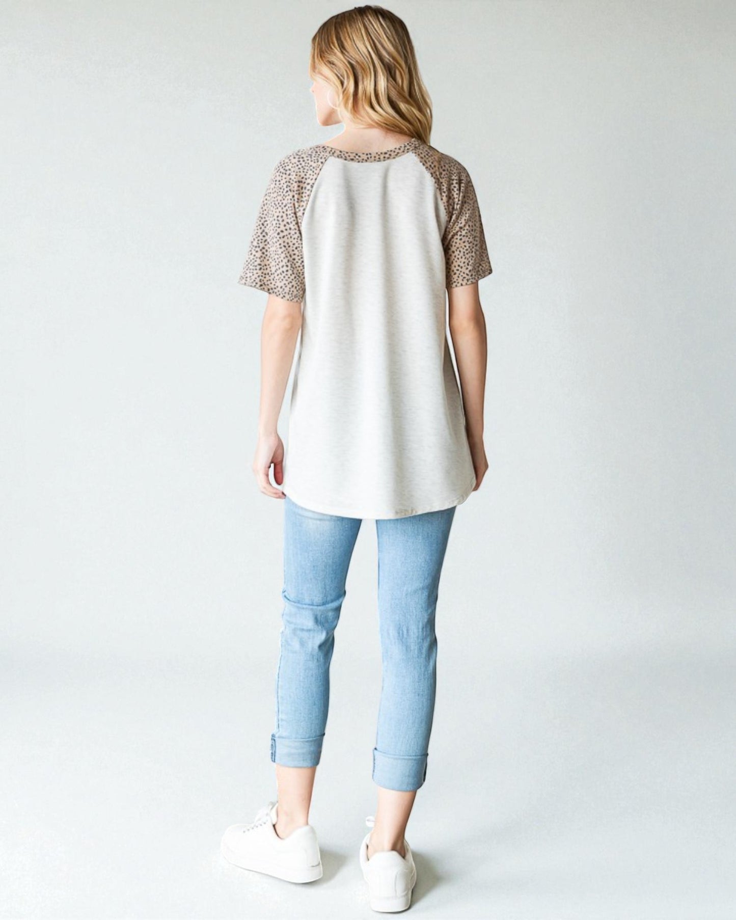 Person wearing a white tunic with brown sleeves and light blue jeans on a plain background