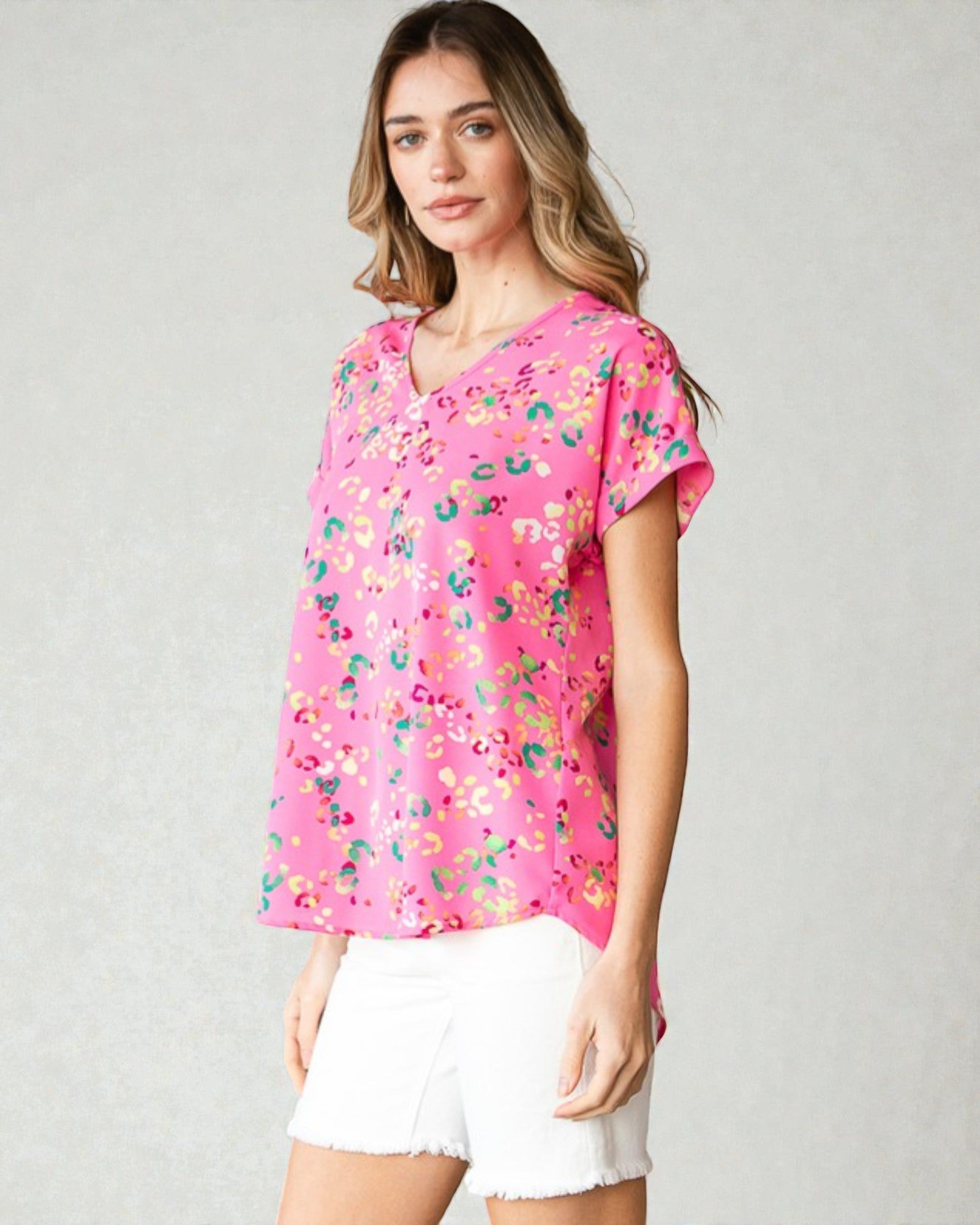 Woman wearing a pink floral blouse and white shorts on a plain background