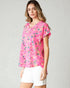 Woman wearing a pink floral blouse and white shorts on a plain background