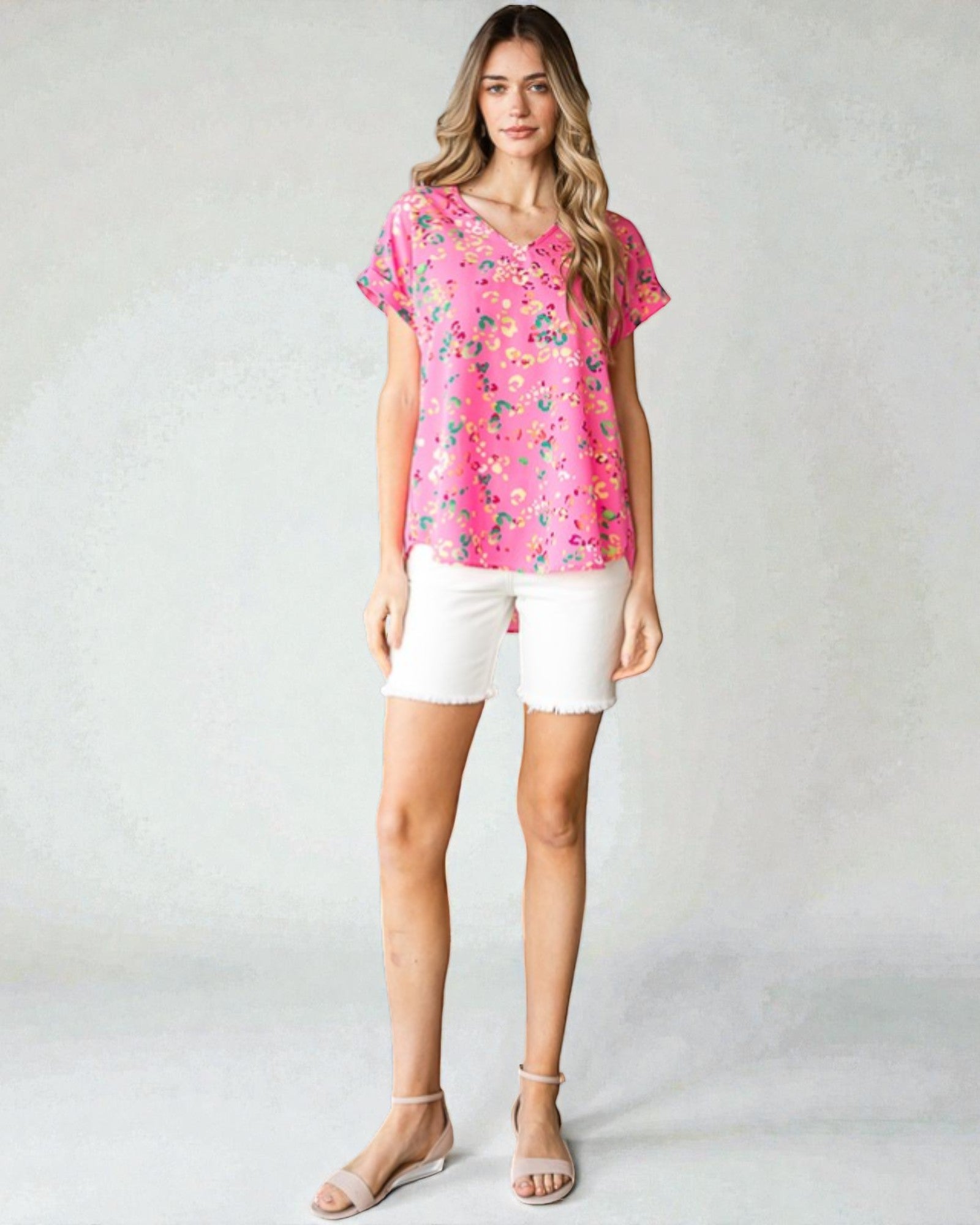 Woman wearing a pink floral blouse and white shorts on a gray background