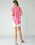 Woman wearing a pink floral blouse and white shorts on a plain background