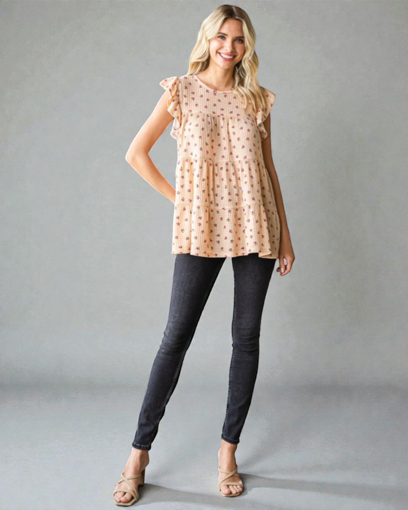 Woman wearing a beige patterned top and dark jeans on a gray background