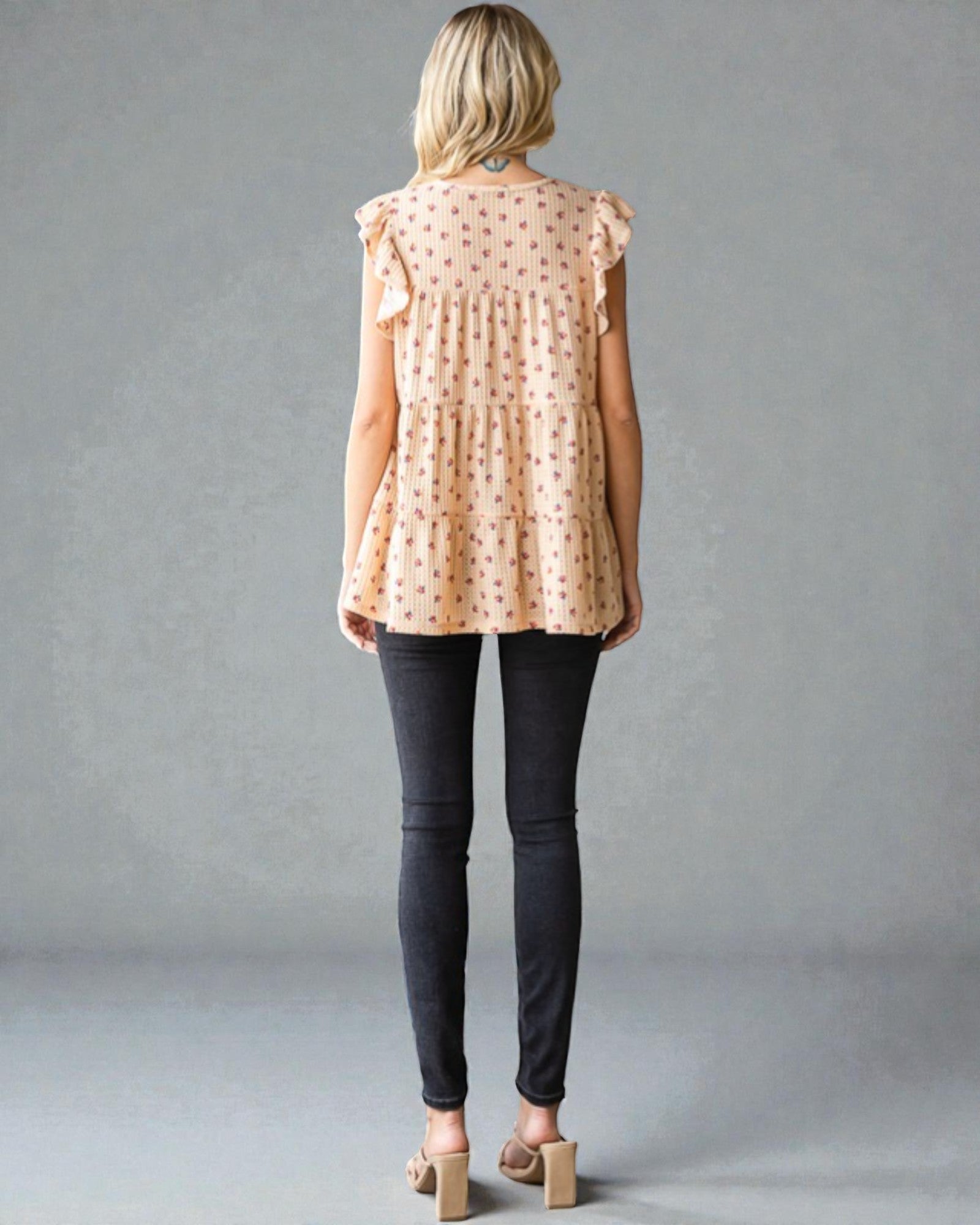 Woman wearing a patterned blouse and dark pants against a gray background