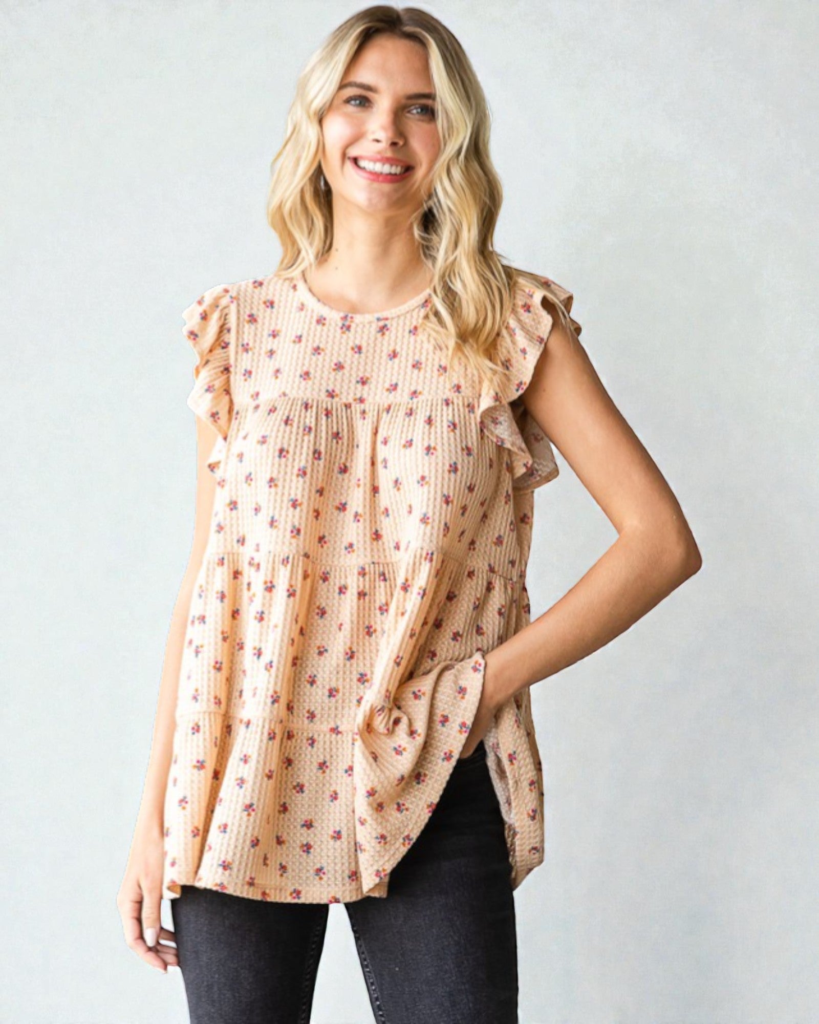 Woman wearing a beige floral blouse with ruffled sleeves against a plain background
