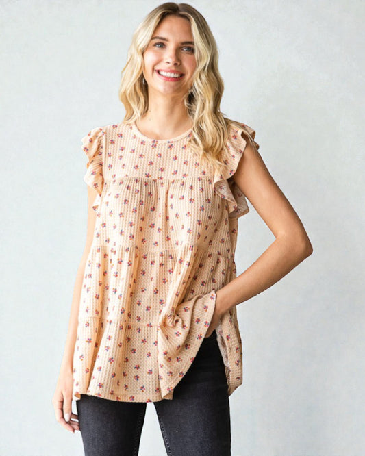 Woman wearing a beige floral blouse with ruffled sleeves against a plain background