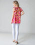 Woman wearing a colorful floral top and white pants on a plain background