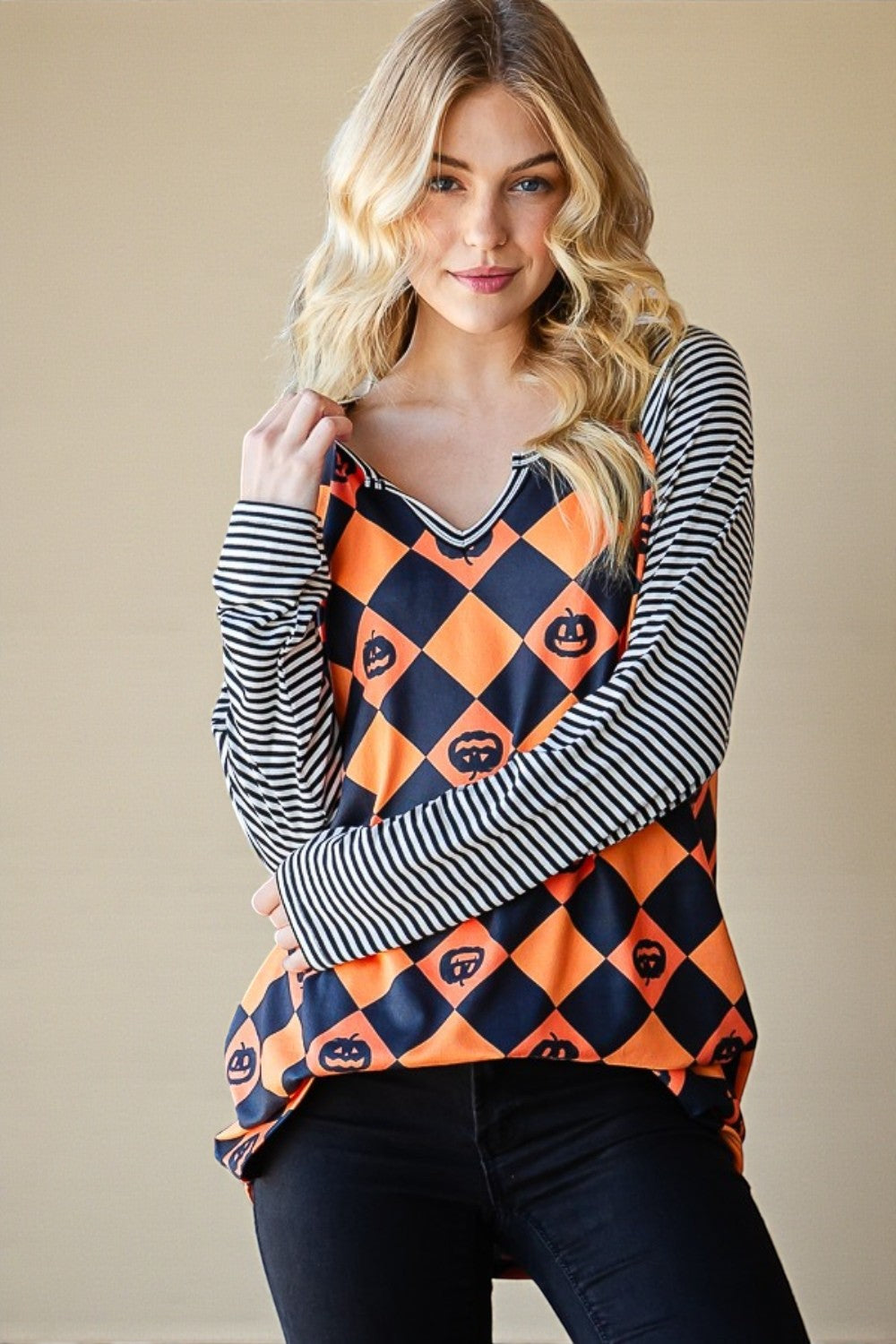 Woman wearing a Halloween-themed top with pumpkins and ghosts, standing against a beige background.