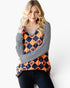 A woman modeling a long-sleeve top with a navy and orange harlequin pattern featuring small jack-o'-lantern motifs, layered over a black and white striped long-sleeve shirt, paired with black jeans against a plain white background.