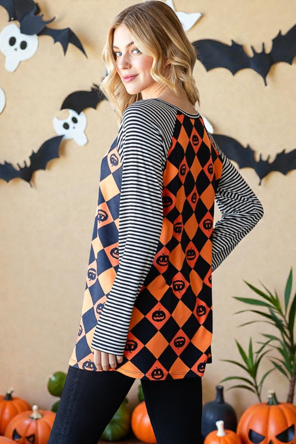 Woman wearing a Halloween-themed dress with pumpkins and ghosts in a decorated room.