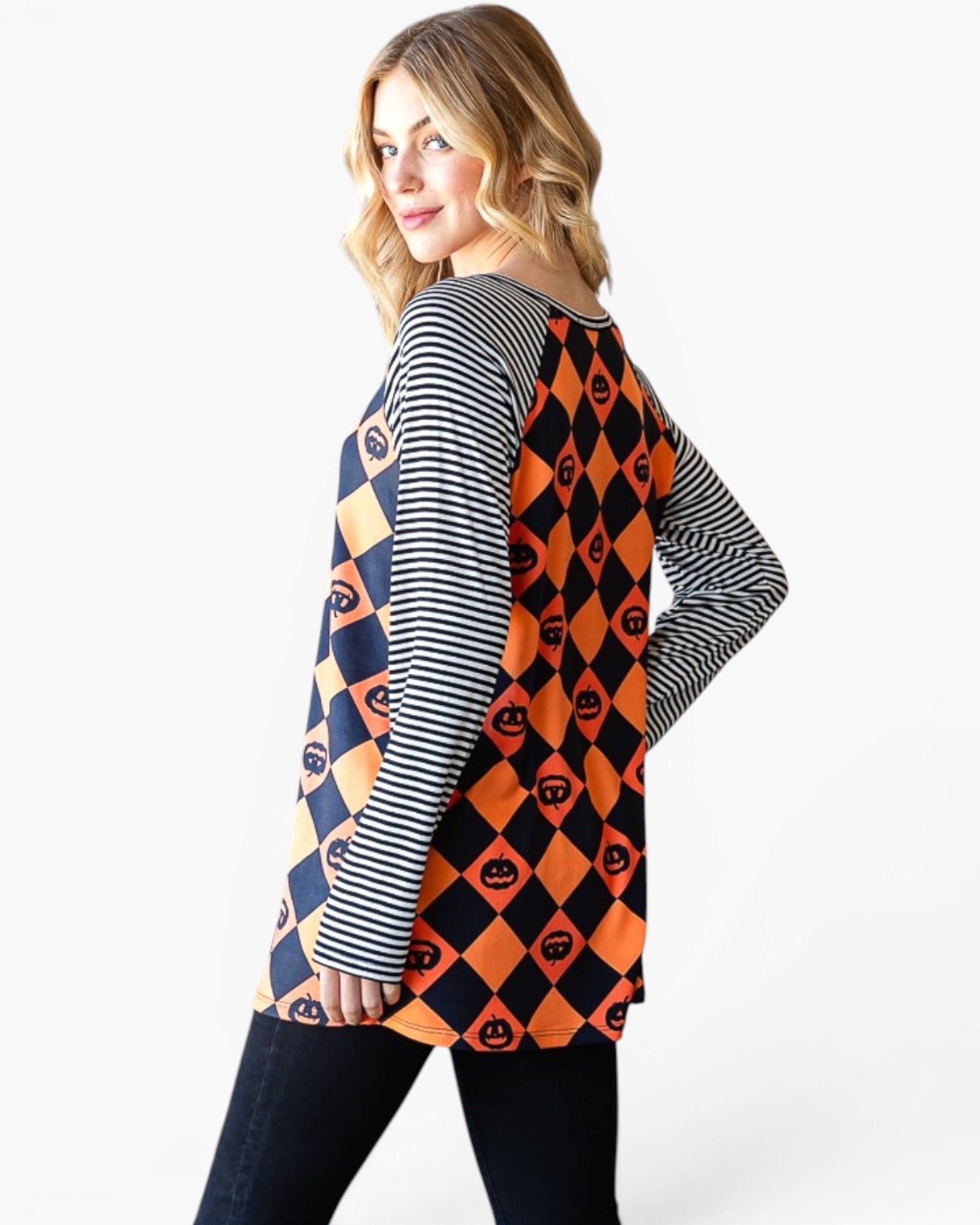 A woman modeling a long-sleeve tunic top with a split design: one side has navy and orange harlequin diamonds with pumpkin motifs, and the other side has navy and white stripes. She is shown from a three-quarter back view against a plain white studio background.