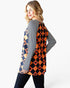 A woman modeling a long-sleeve tunic top with a split design: one side has navy and orange harlequin diamonds with pumpkin motifs, and the other side has navy and white stripes. She is shown from a three-quarter back view against a plain white studio background.