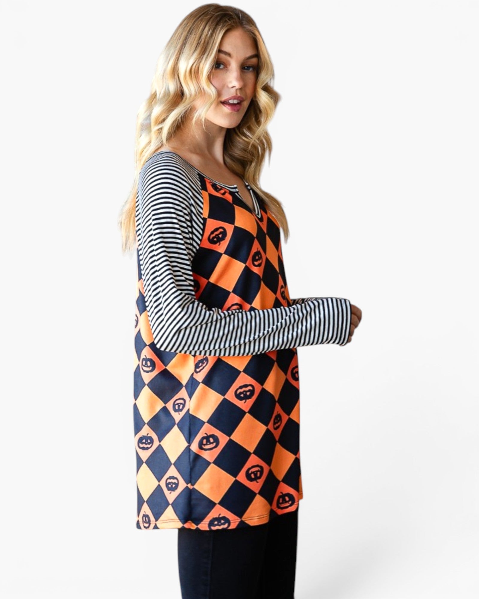 A woman modeling a long-sleeve tunic top with a navy and orange harlequin pattern featuring jack-o'-lantern motifs, layered over a navy and white striped long-sleeve shirt, against a light gray background.