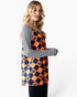 A woman modeling a long-sleeve tunic top with a navy and orange harlequin pattern featuring jack-o'-lantern motifs, layered over a navy and white striped long-sleeve shirt, against a light gray background.