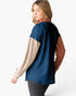 A woman shown from the back wearing a color-blocked long-sleeve top with a navy blue main body, beige sleeves, and rust brown sleeves, paired with dark gray pants against a clean white background.