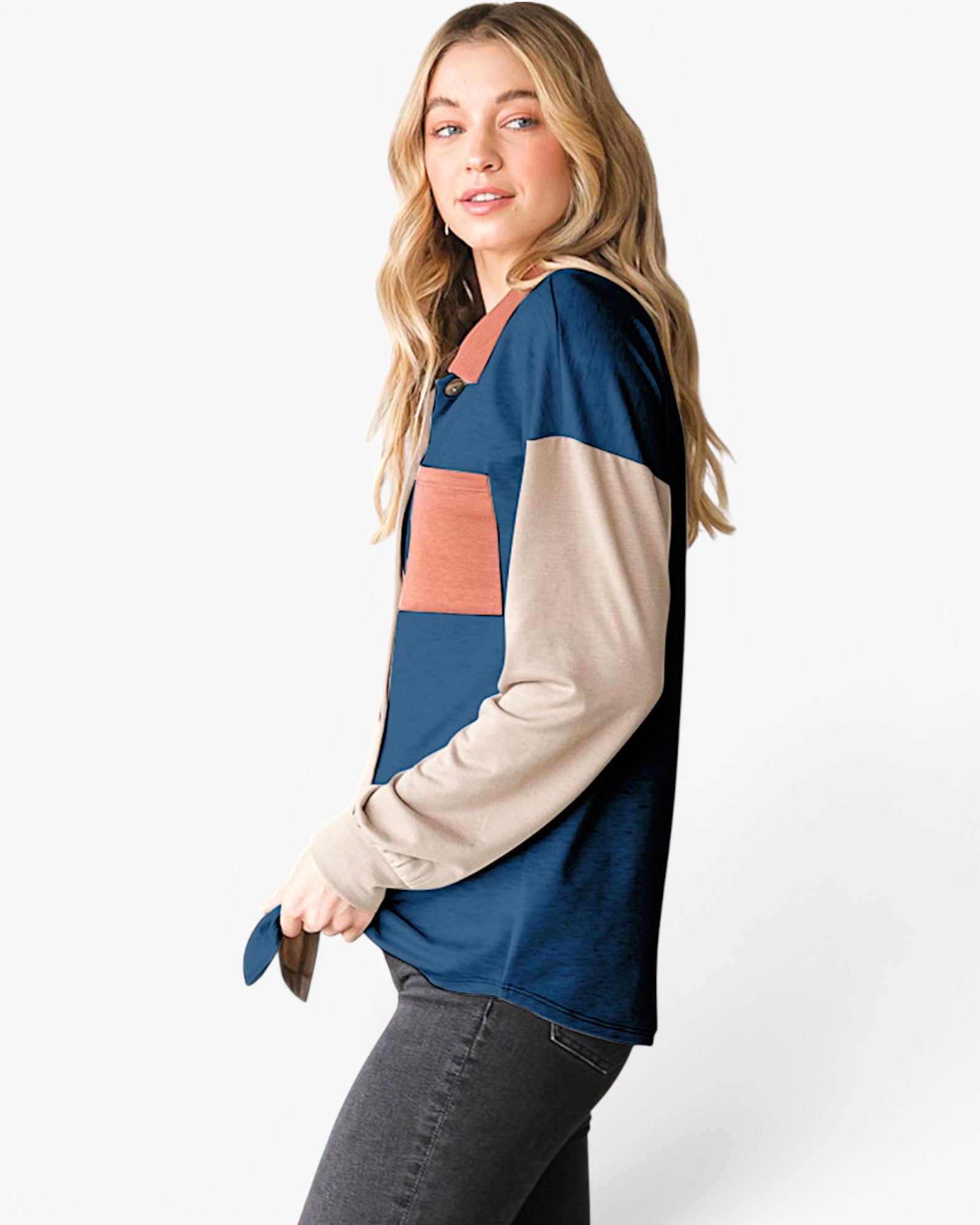 A woman modeling a color-block long-sleeve top with navy blue, beige, and dusty rose panels, paired with dark gray jeans against a plain white studio background.