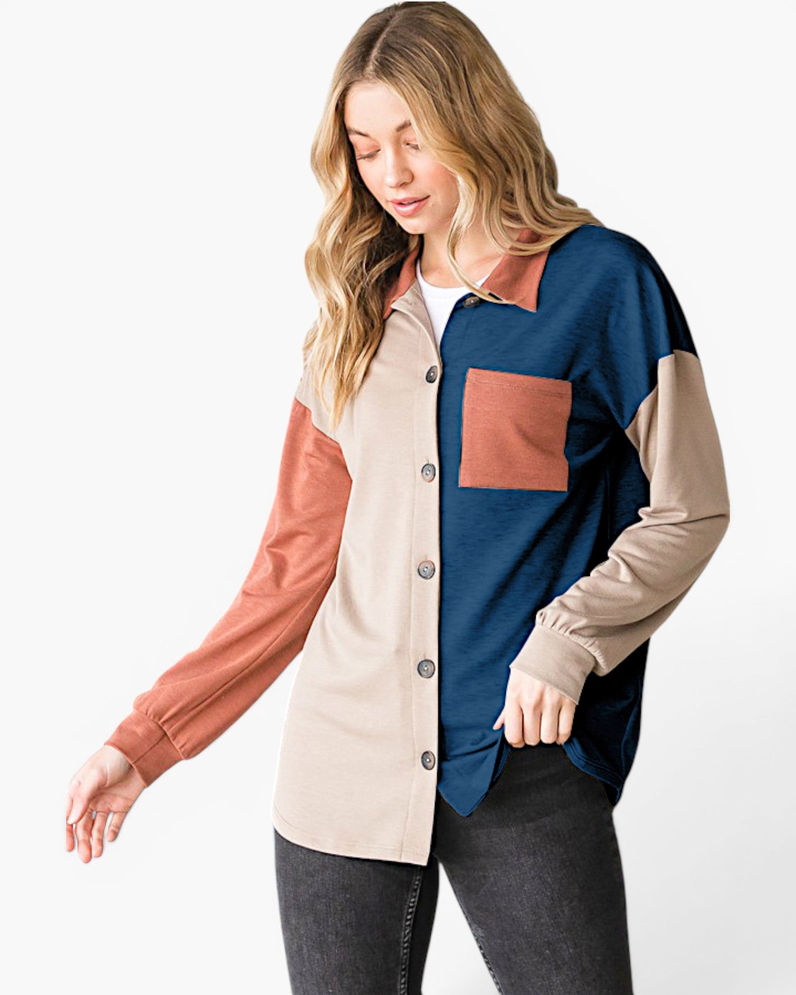 A woman modeling a color-block long-sleeve button-up shirt with navy, beige, and terracotta panels, paired with dark gray jeans against a plain white studio background.
