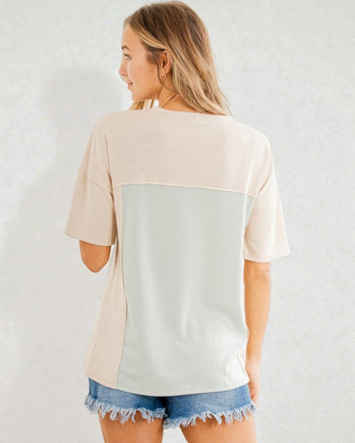 Woman wearing a beige and light gray color-blocked top with denim shorts on a white background