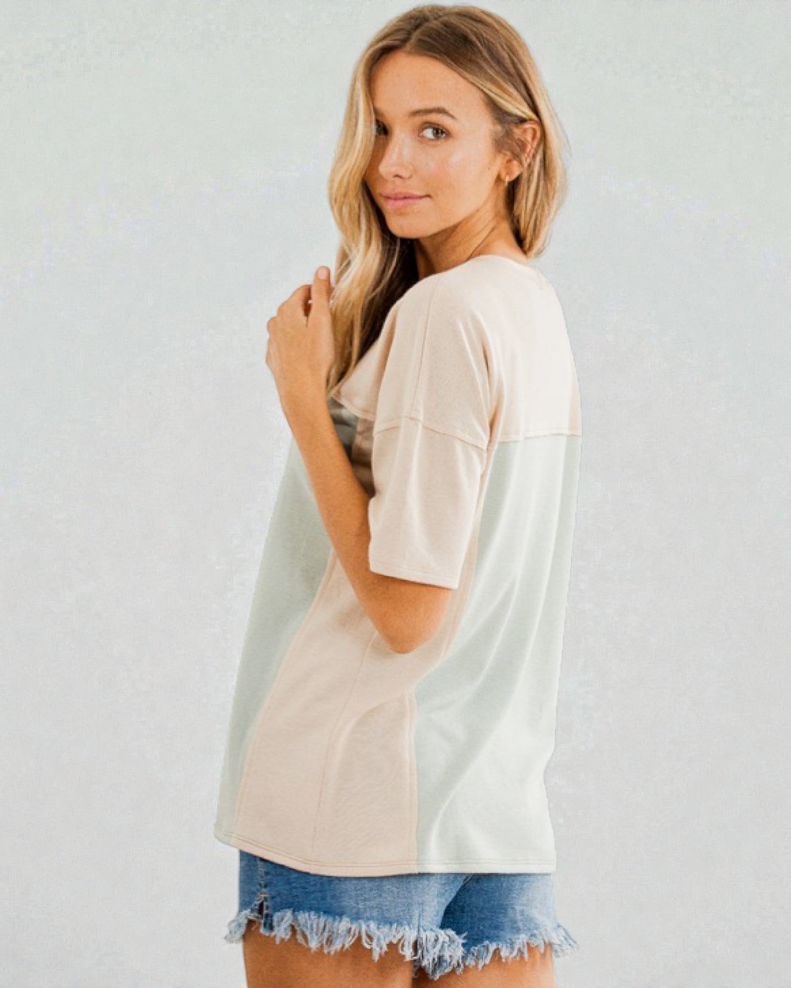 Woman wearing a beige and white color-blocked top with a denim skirt on a plain background