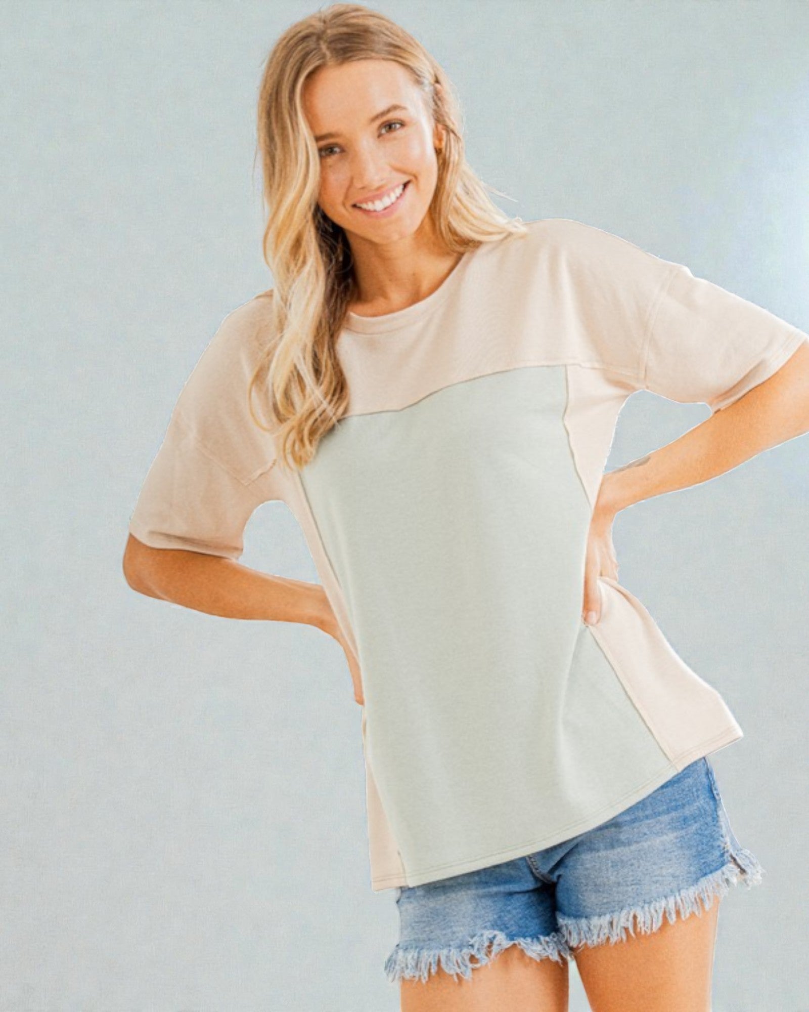 Woman wearing a beige and light green color-blocked top with denim shorts on a plain background