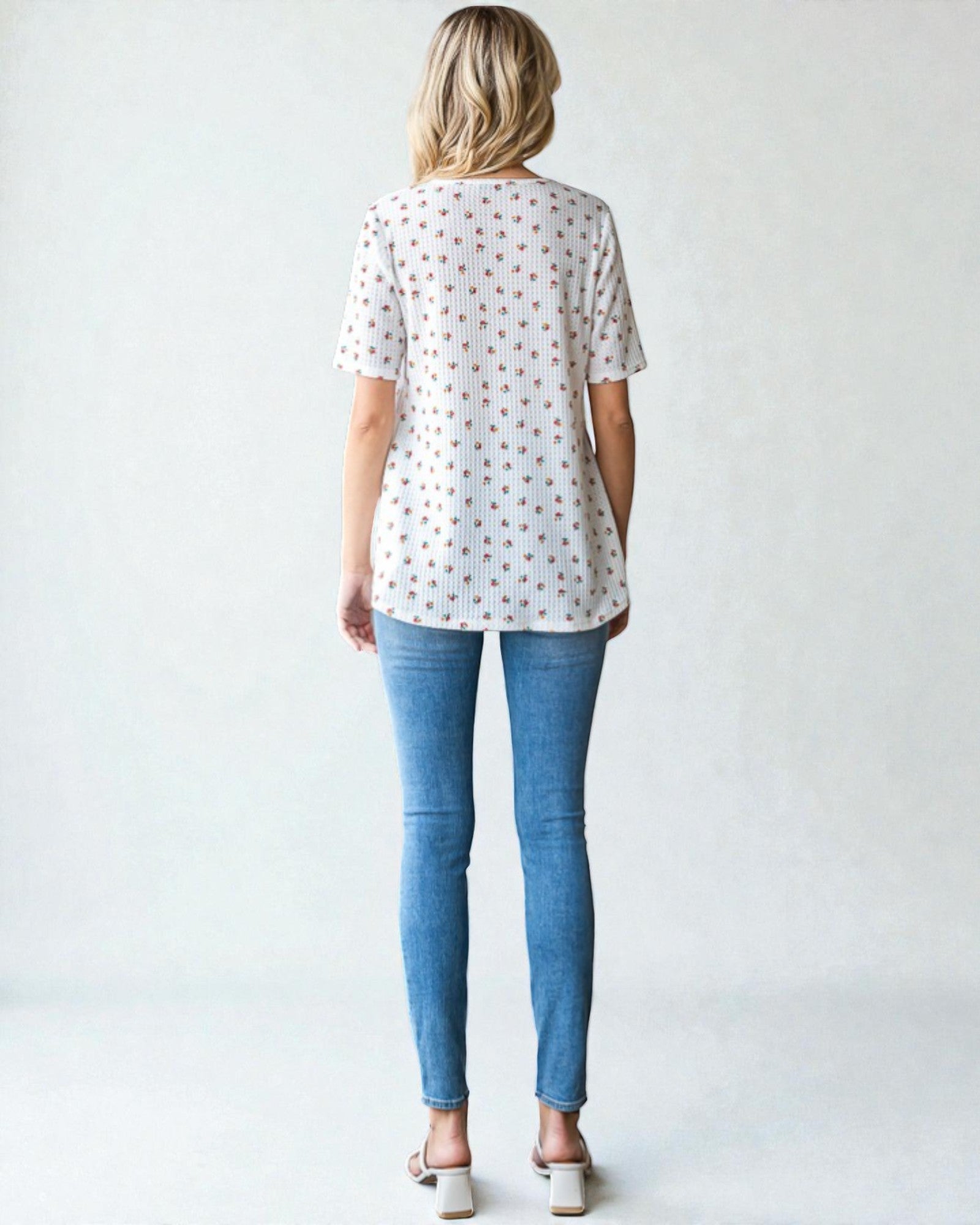 Woman wearing a white blouse with small patterns and blue jeans on a plain background