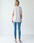 Woman wearing a white blouse with small patterns and blue jeans on a plain background