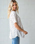 Woman wearing a white floral blouse and blue jeans against a light tiled wall.