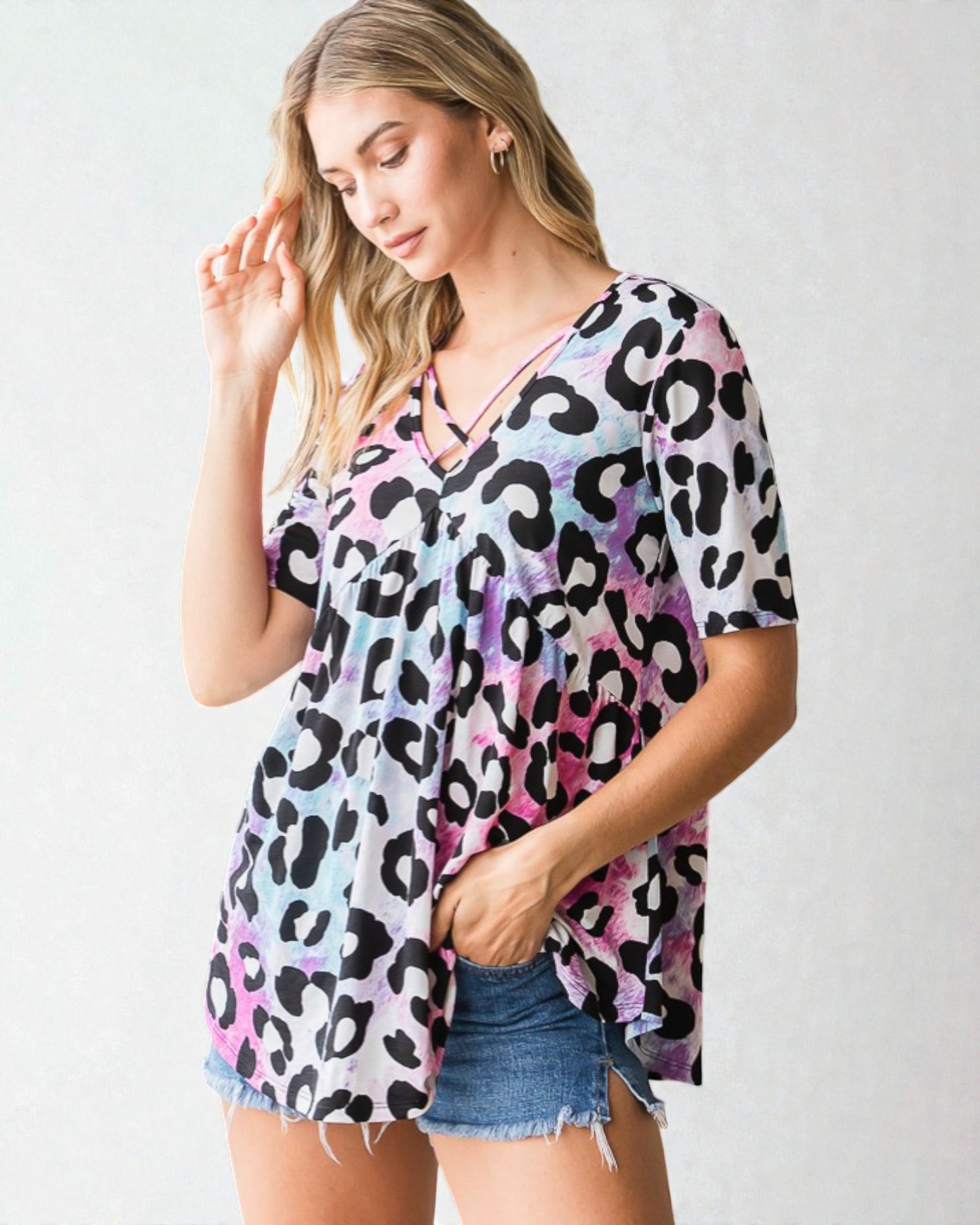 Woman wearing a colorful leopard print top and denim shorts on a white background