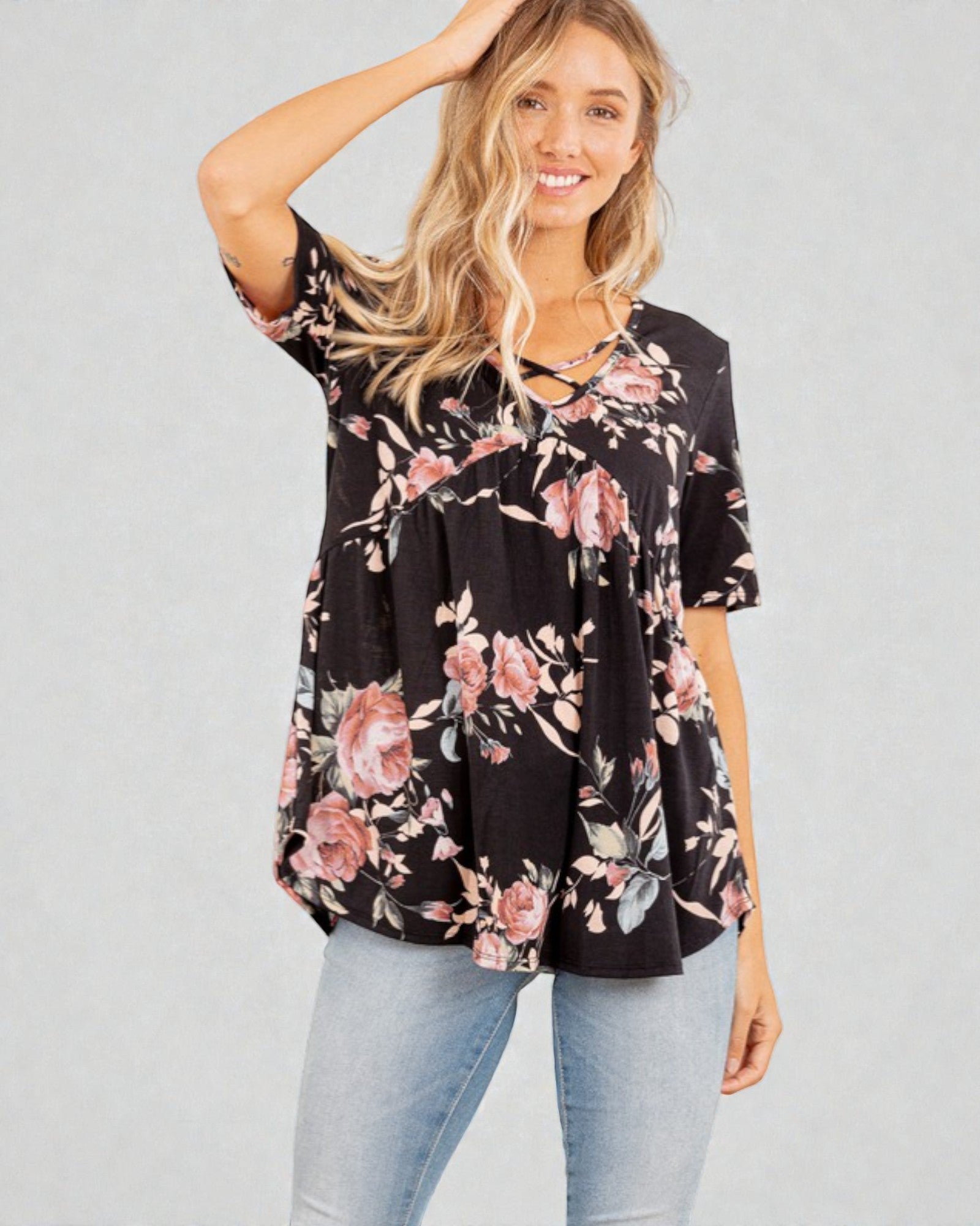 Woman wearing a black floral blouse with light blue jeans on a gray background