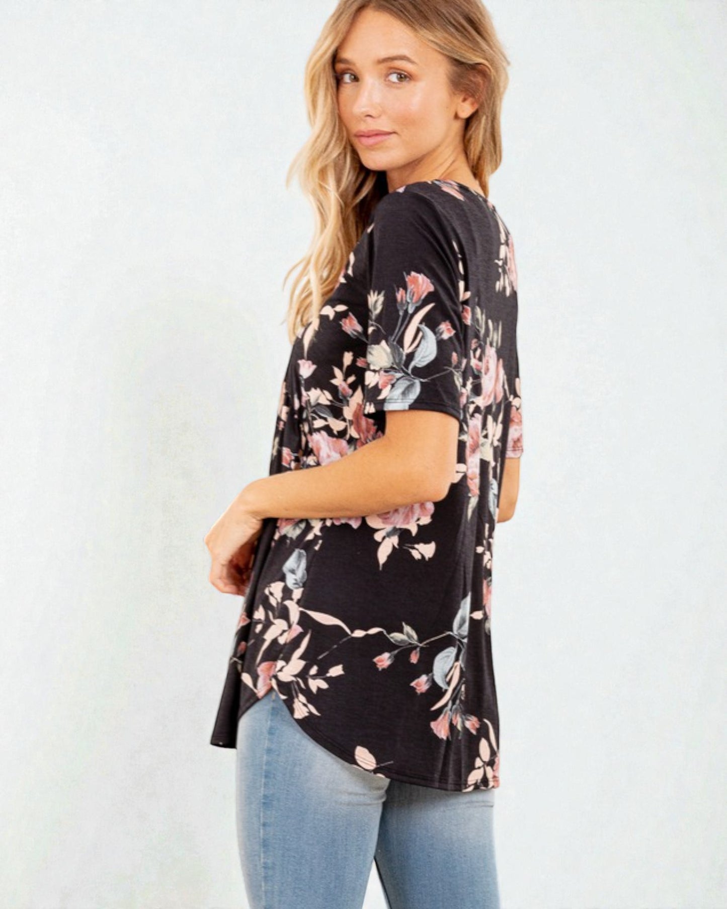 Woman wearing a black floral top and light blue jeans on a white background