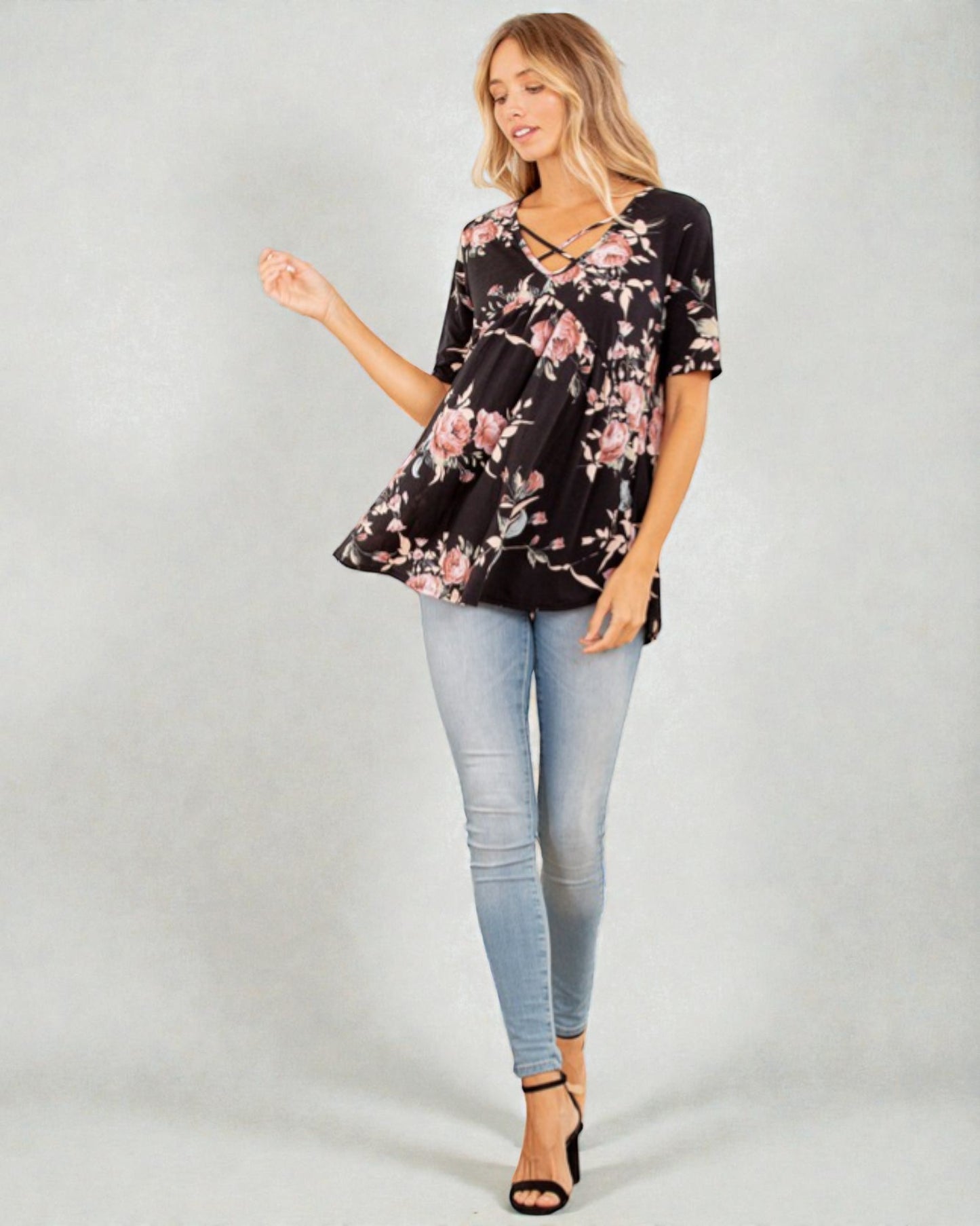 Woman wearing a black floral top and light blue jeans on a gray background