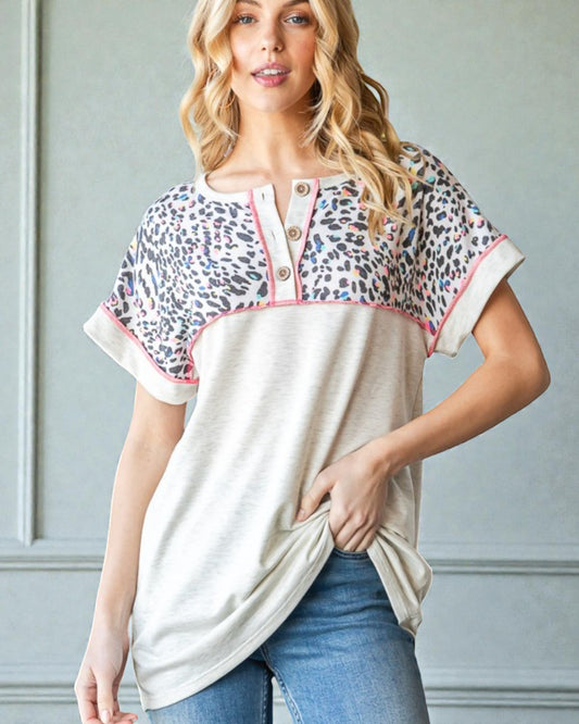 Woman wearing a leopard print and beige top with blue jeans against a gray wall.