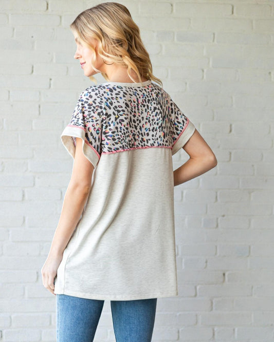 Woman wearing a light-colored tunic with leopard print sleeves against a white brick wall.